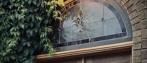 Una ventana de arco de piedra con un diseño de vitral, rodeada de hiedra y un marco de madera.