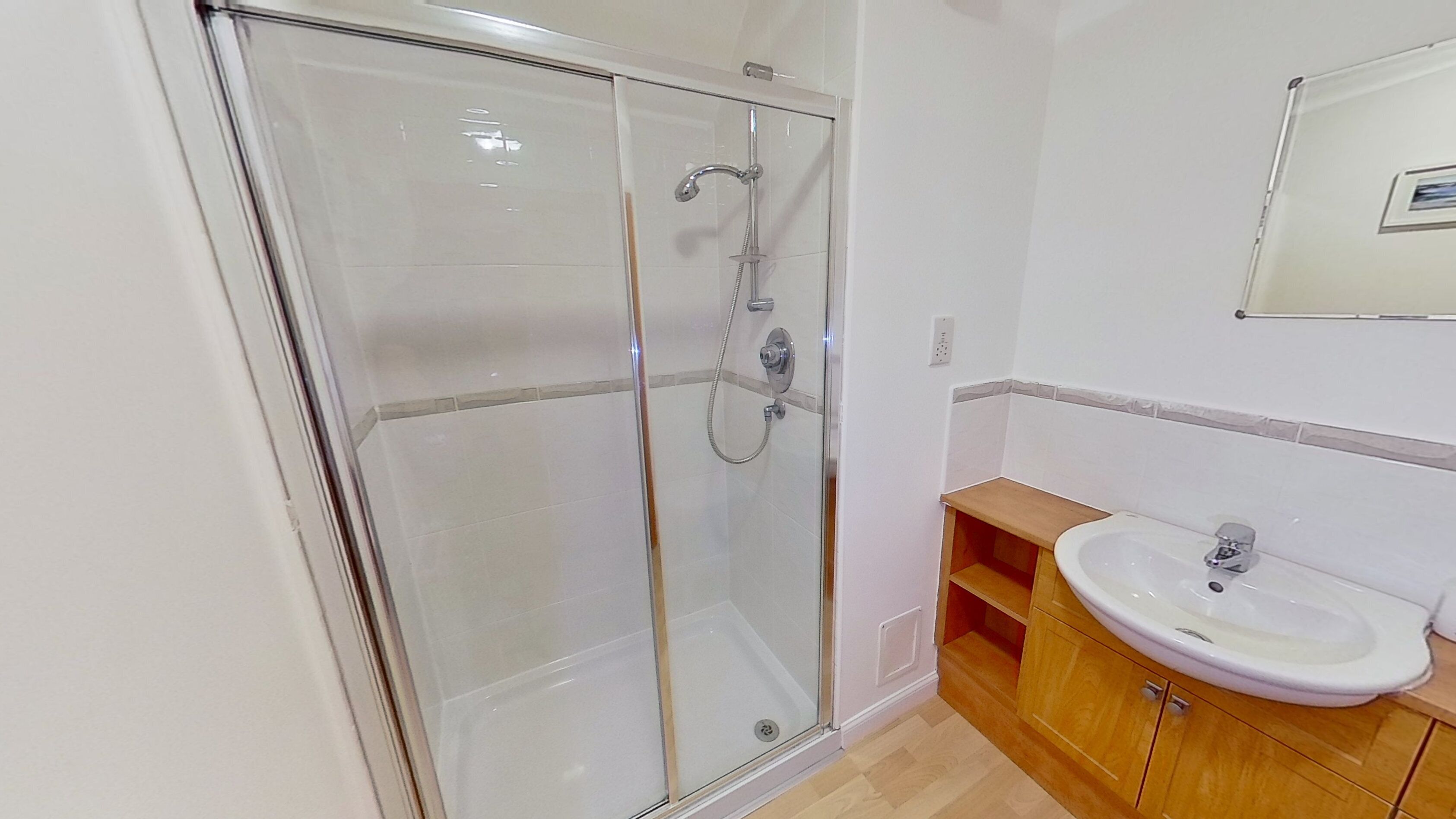 A bathroom with a glass shower enclosure, a wooden vanity with a sink, and a mirror above the sink.