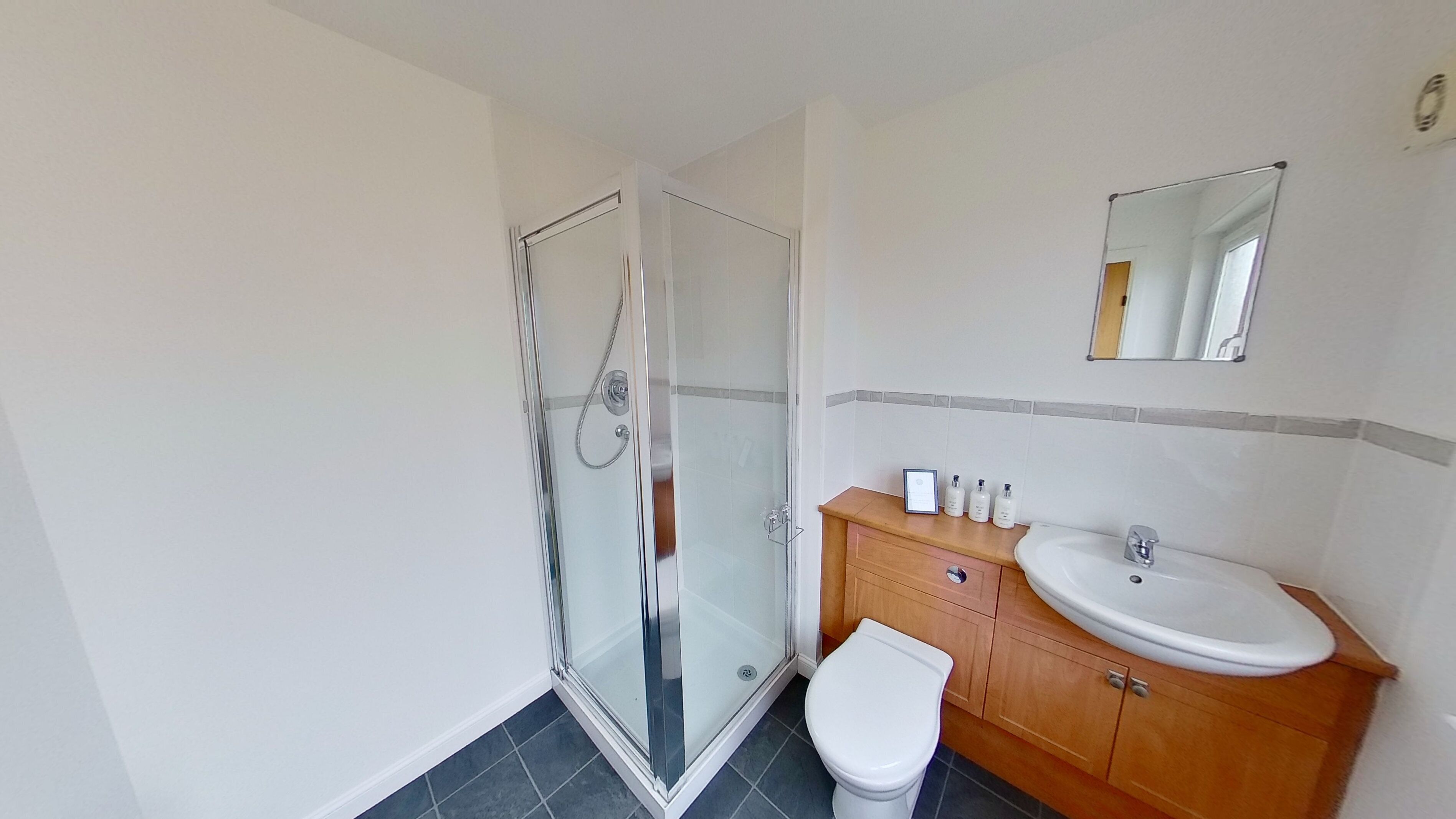 Ein modernes Badezimmer mit einer Duschkabine, einer weißen Toilette und einem Holzwaschtisch mit Spüle und Spiegel.