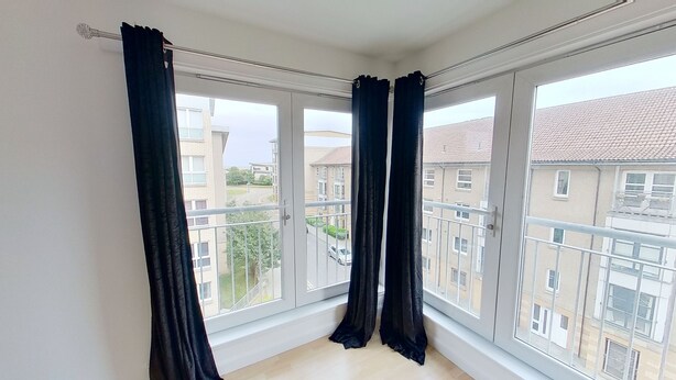 A room with large windows, black curtains, and a view of neighboring buildings. - Orange Apartments Bothwell Road (Aberdeen)