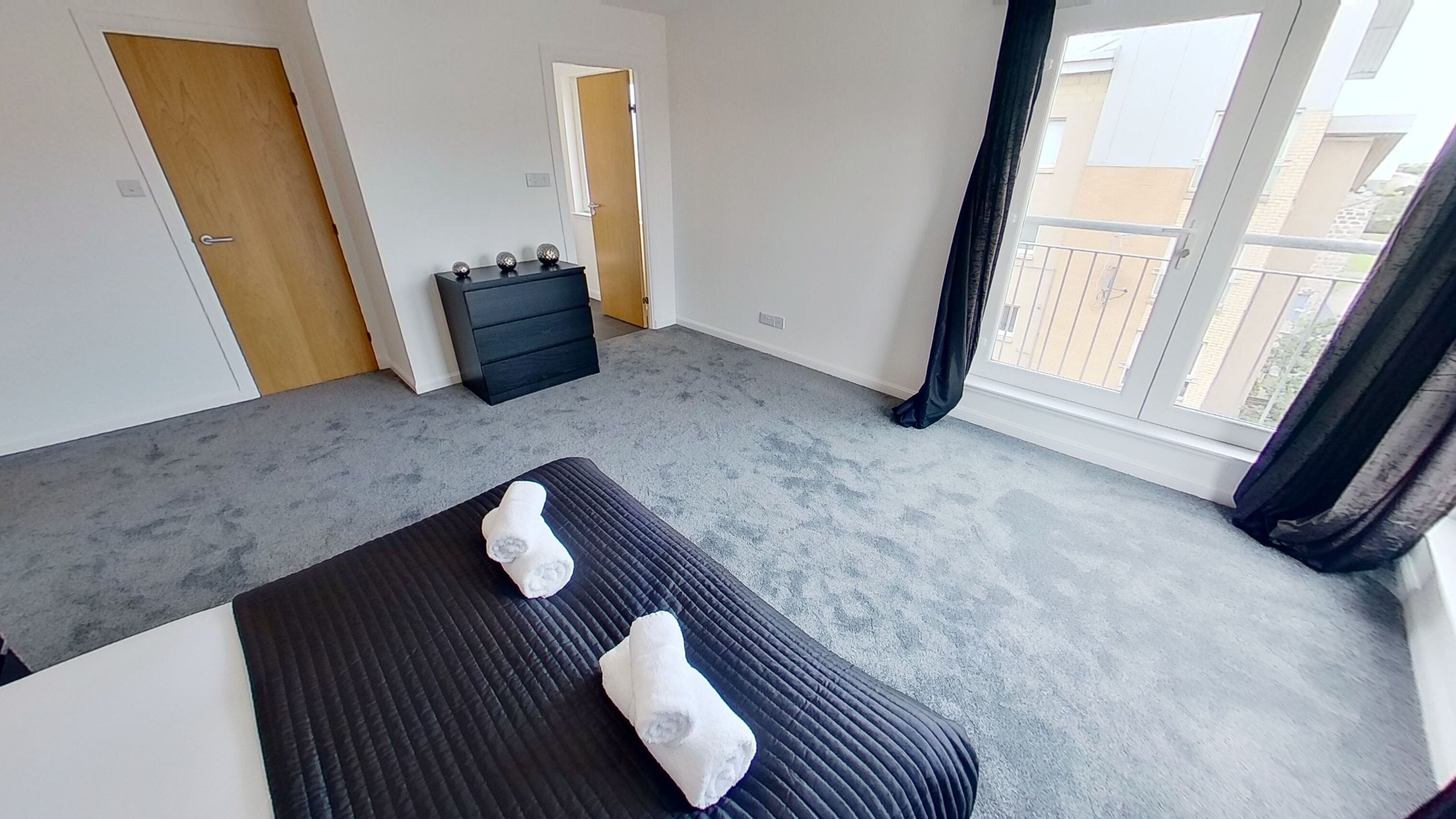 Une chambre avec un grand lit, une commode et une fenêtre donnant sur des immeubles.