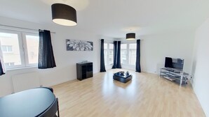 A spacious living room with a large window, a black entertainment unit, a coffee table, and a black chair. - Orange Apartments Bothwell Road (Aberdeen)