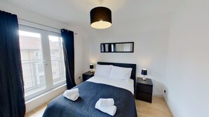 A hotel room with a large bed, two bedside tables with lamps, a window with curtains, a ceiling light, and a mirror on the wall. - Orange Apartments Bothwell Road (Aberdeen)