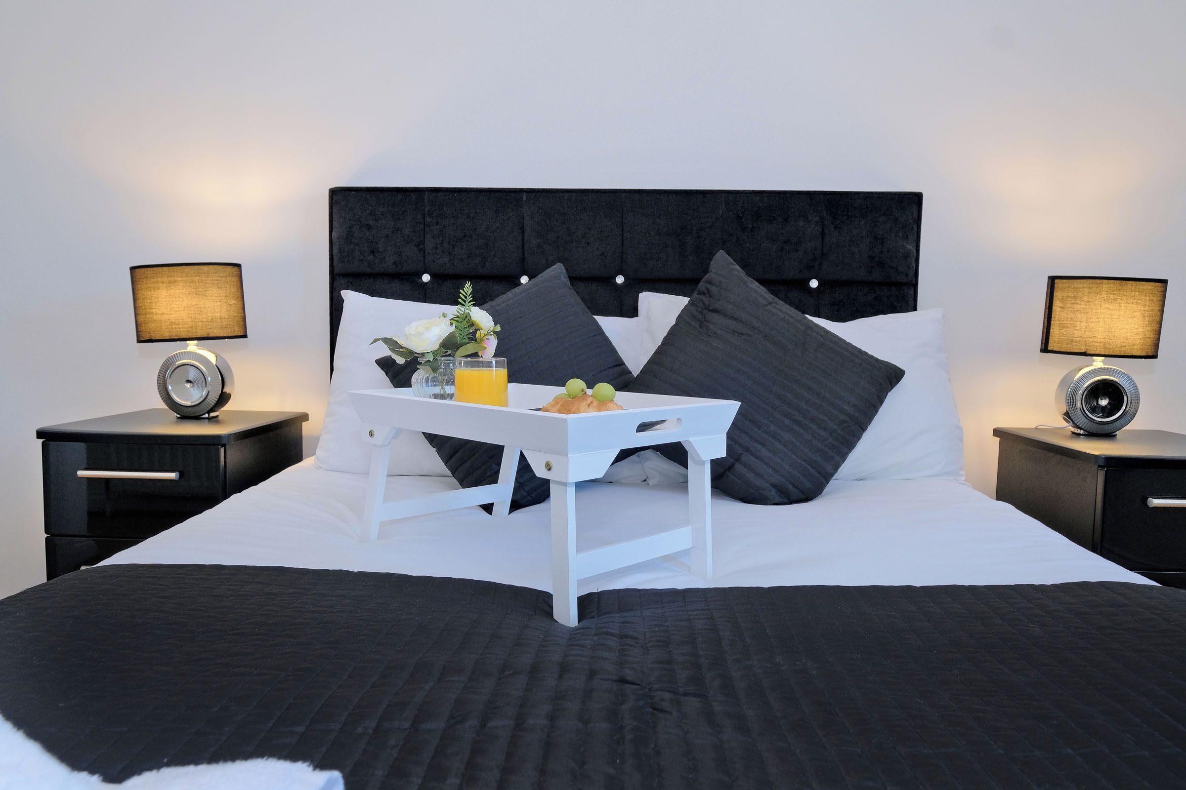 A neatly made bed with a tray of breakfast items, two bedside lamps, and a dark headboard.