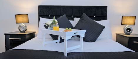 A neatly made bed with a tray of breakfast items, two bedside lamps, and a dark headboard.