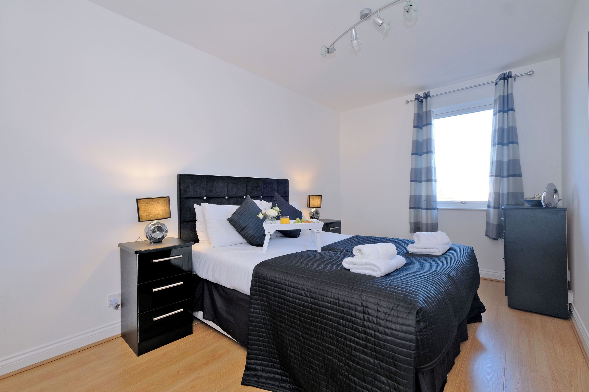 A modern bedroom with a large bed, bedside tables, a dresser, and a window with curtains.