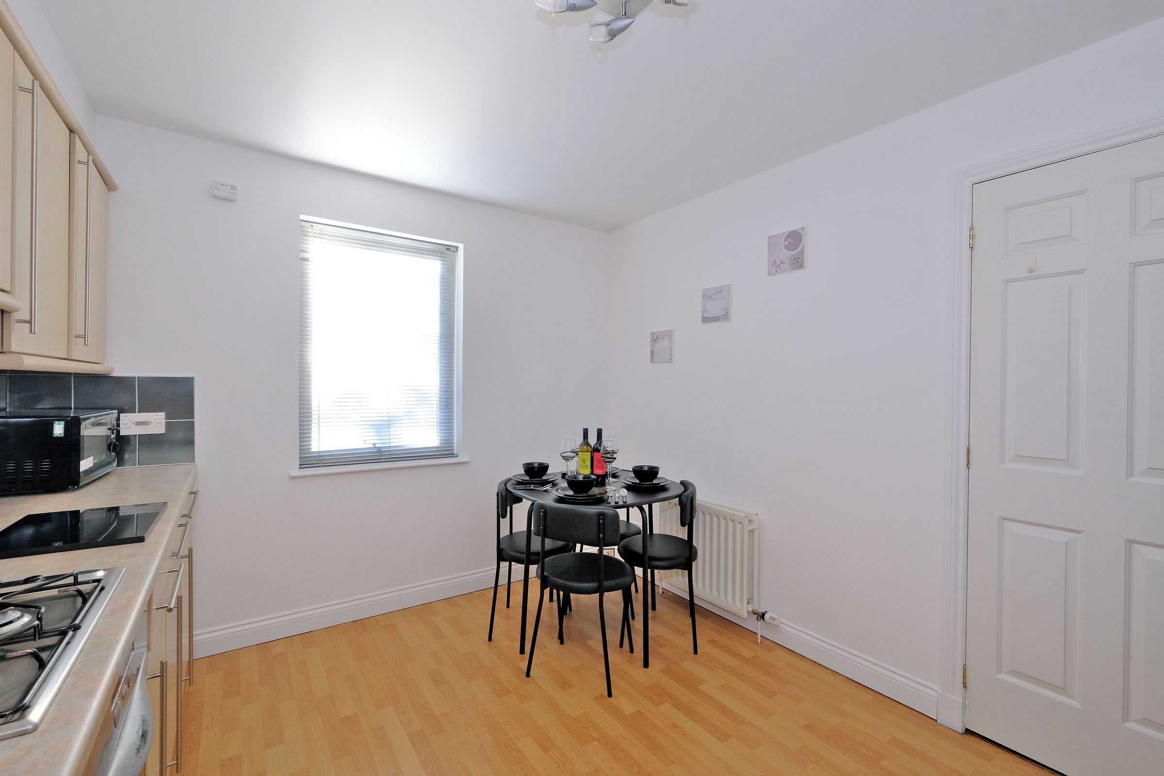 A compact kitchen with a dining area, featuring a stove, microwave, and a table set for two with chairs.