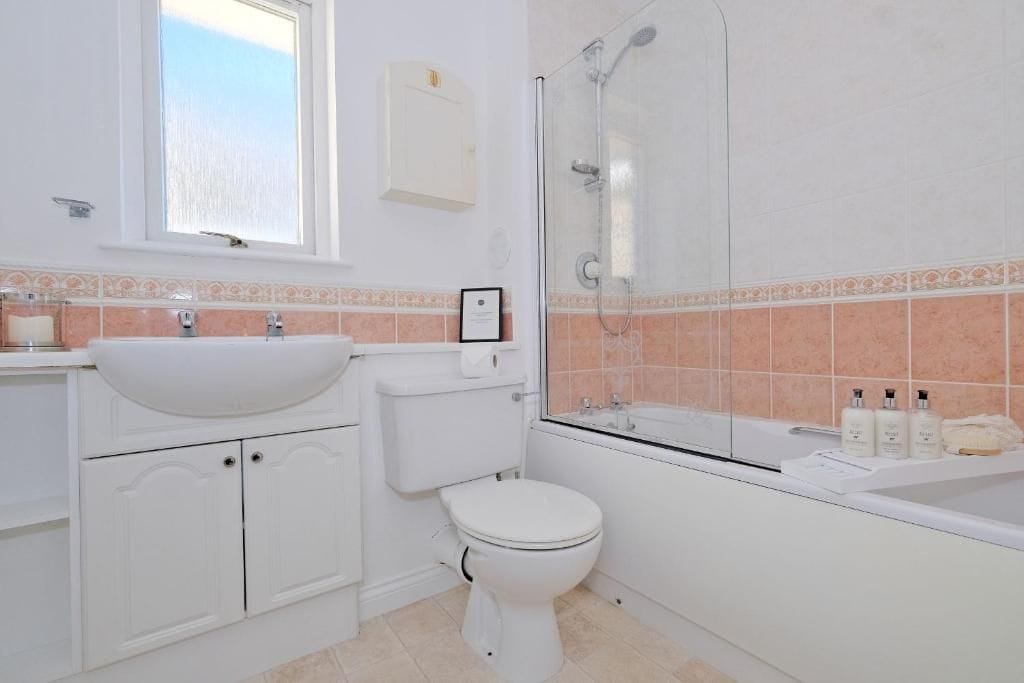 A bathroom with a white sink, toilet, and shower. There is a window above the sink and a cabinet below.