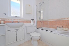 A bathroom with a white sink, toilet, and shower. There is a window above the sink and a cabinet below. - Orange Apartments Beechgrove (Aberdeen)