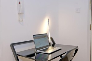 A laptop on a glass table with a chair, a wall-mounted telephone, and a light switch. - Orange Apartments Beechgrove (Aberdeen)