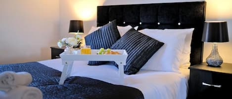 A hotel room with a bed, a bedside table with a tray of fruit, a lamp, and a vase.