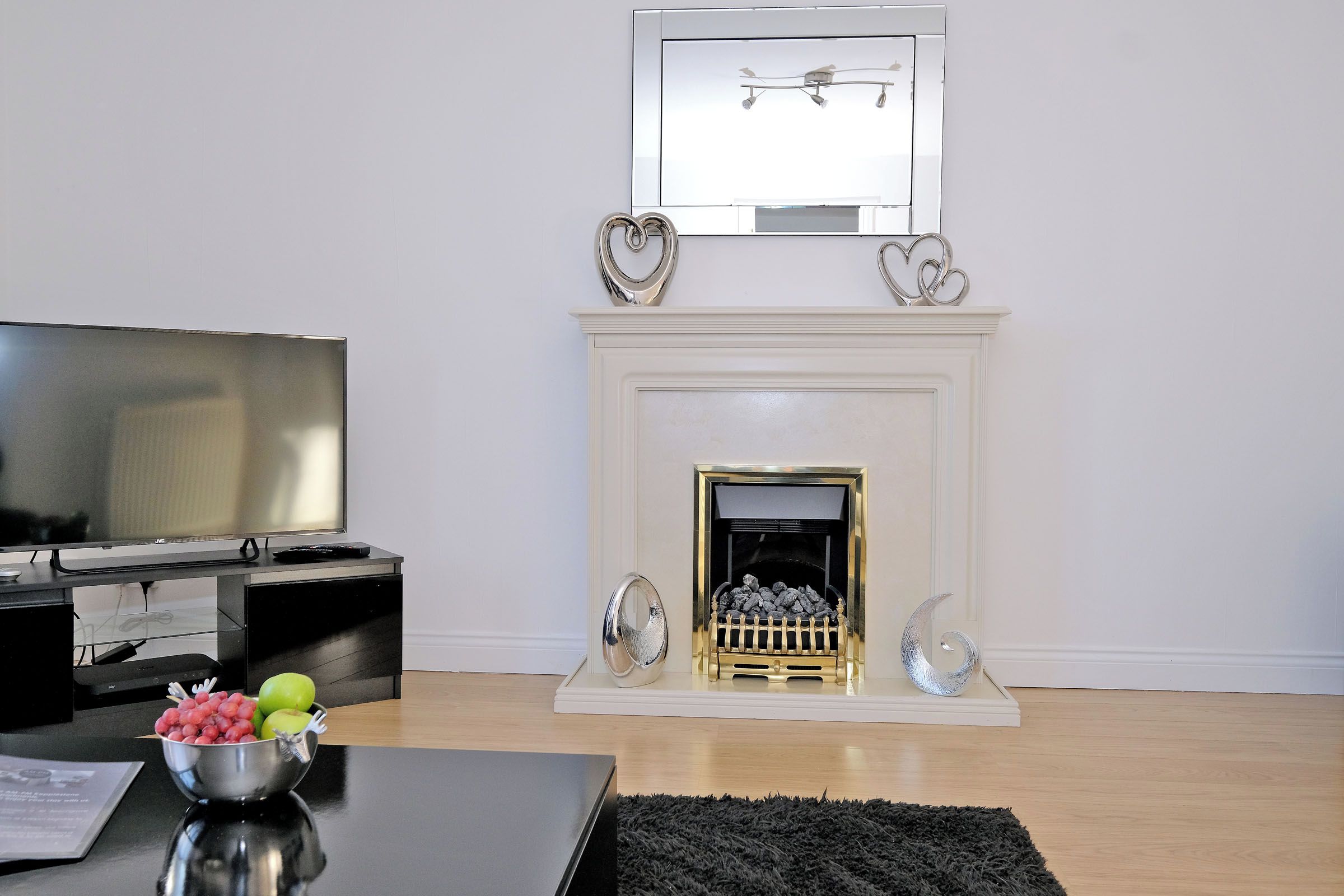 A living room with a flat-screen TV, a fireplace with decorative items, and a bowl of fruit on a table.
