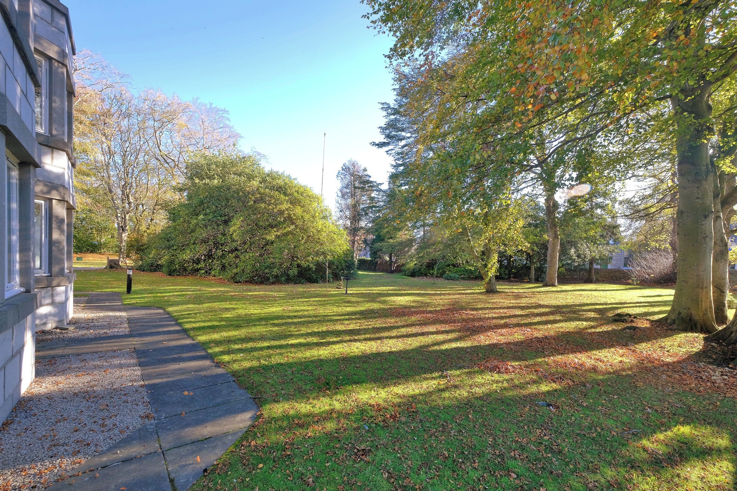 A well-maintained grassy area with a paved walkway, surrounded by trees and a building.