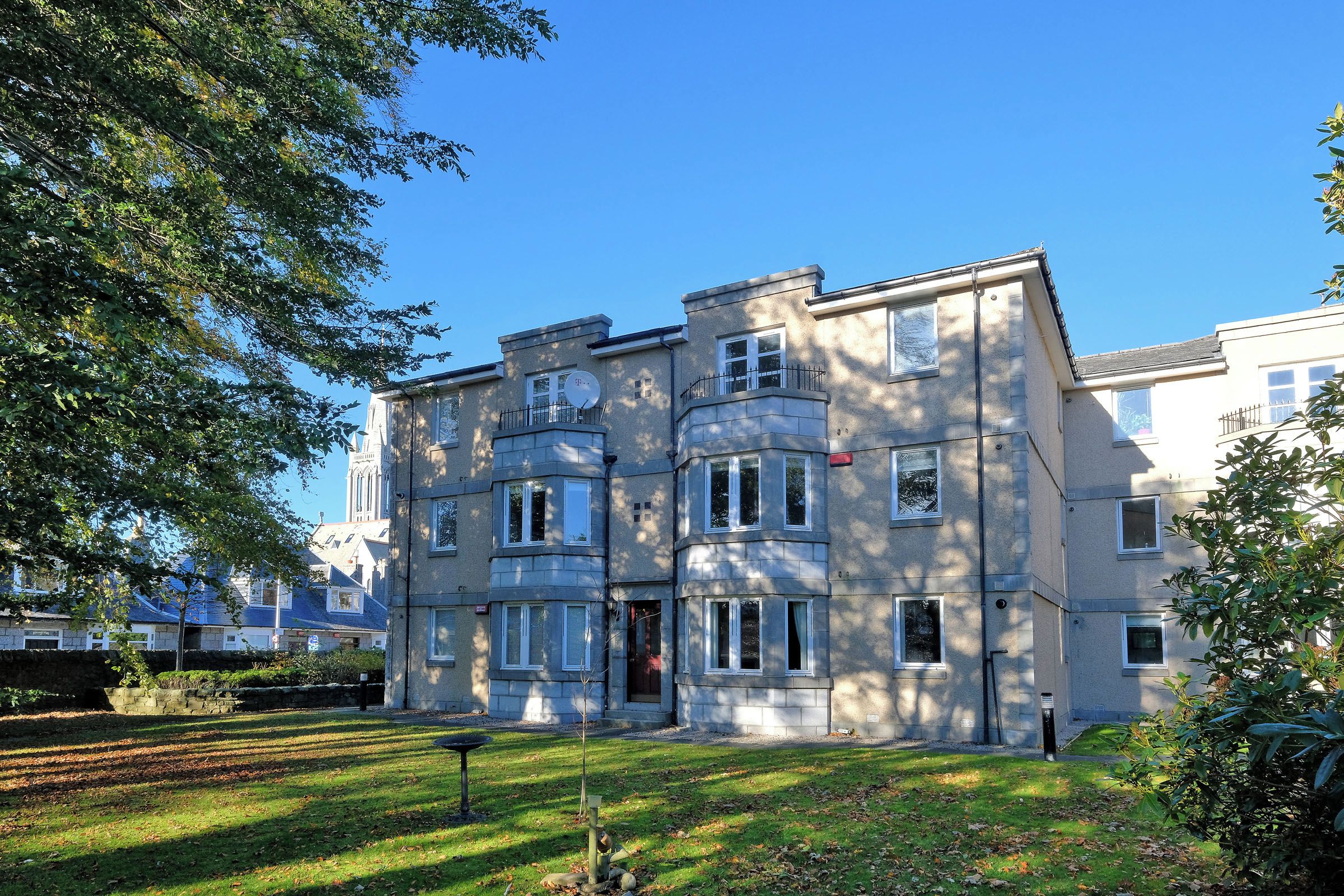 A multi-story residential building with a symmetrical facade, large windows, and a well-maintained lawn.