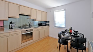 A modern kitchen with light wood cabinets, a gas stove, a microwave, and a dining area with black chairs and a table set for four. - Orange Apartments Beechgrove (Aberdeen)
