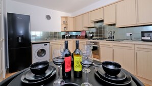 A modern kitchen with a black refrigerator, washing machine, and a dining area with wine glasses and bottles. - Orange Apartments Beechgrove (Aberdeen)