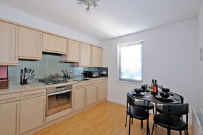 A modern kitchen with light wood cabinets, a gas stove, a microwave, and a dining area with a table set for four. - Orange Apartments Beechgrove (Aberdeen)