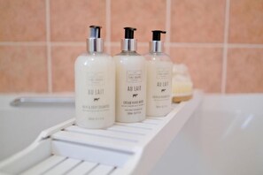 Three bottles of 'AU LAIT' body wash on a white shelf in a bathroom. - Orange Apartments Beechgrove (Aberdeen)