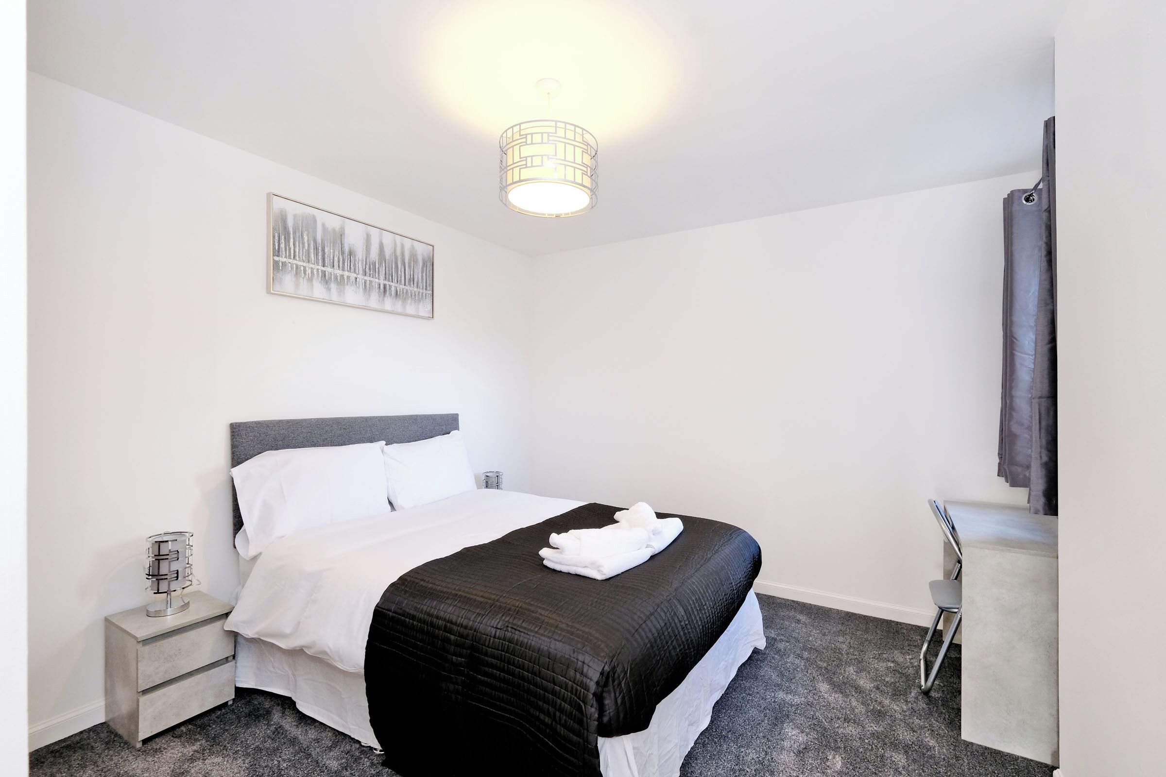 A neatly made bed with a black and white duvet, a bedside table with a lamp, and a painting on the wall.