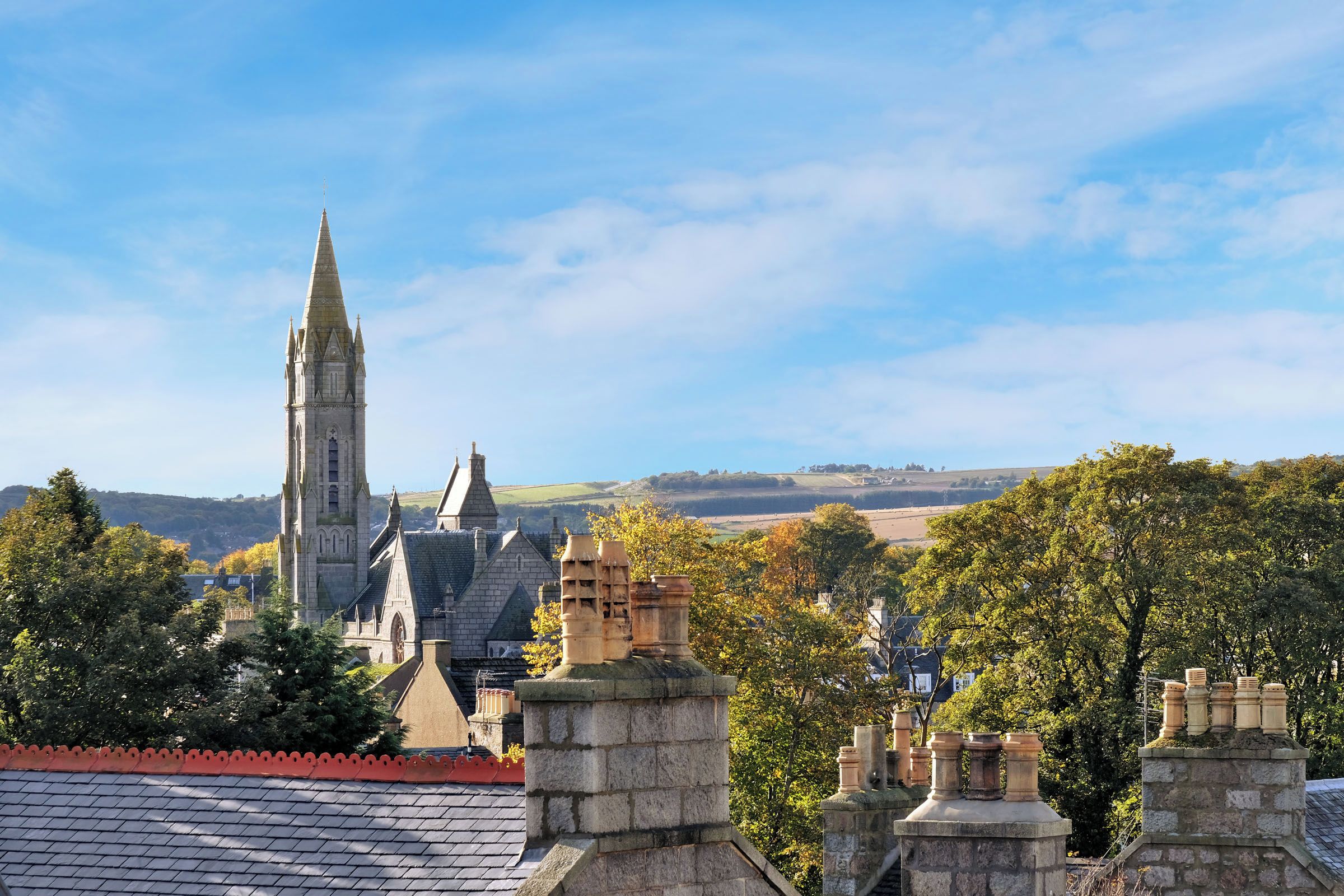 A historic building with a prominent tower and multiple spires, surrounded by trees and a clear sky.