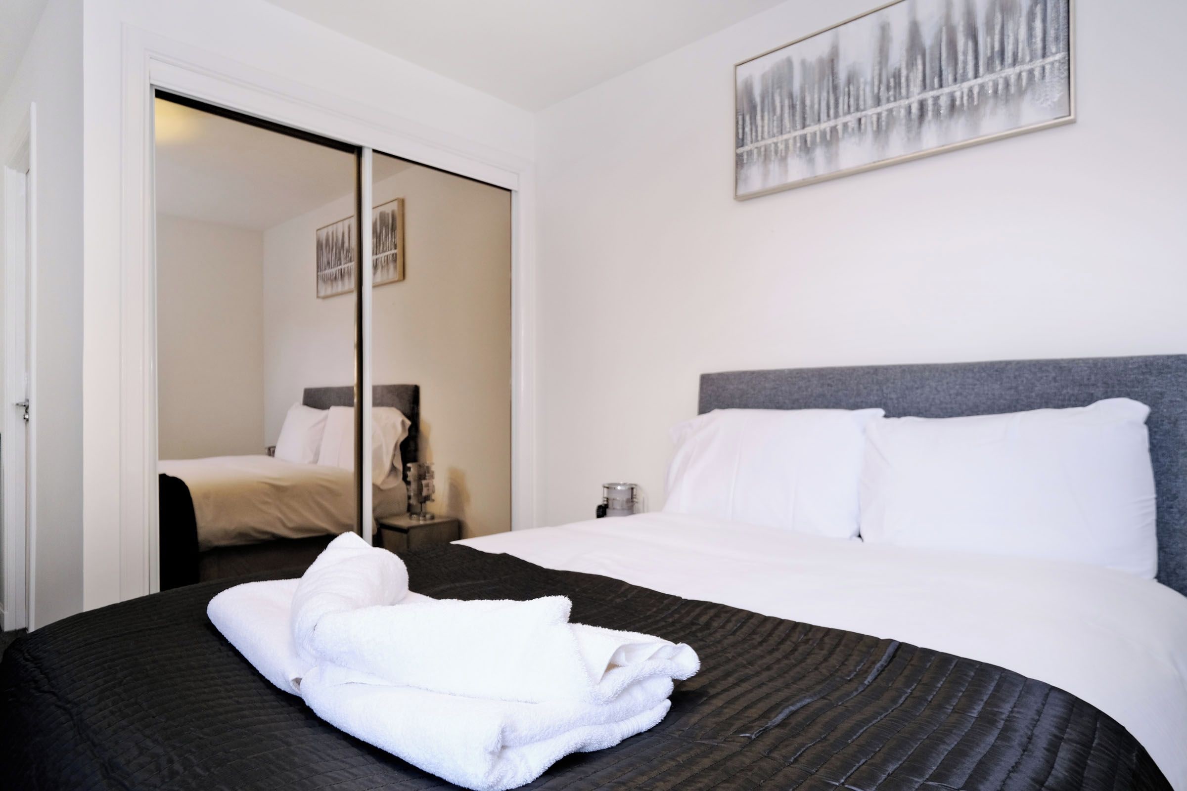 A hotel room with a bed, a bedside table, a mirror, and a painting on the wall.