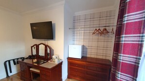 A bedroom with a wooden dresser, a television, a mirror, and a bed with a red plaid curtain. - Midway Guest House (Torquay)