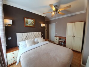 A bedroom with a large bed, a ceiling fan, a desk with drawers, a wardrobe, and a painting on the wall. - Midway Guest House (Torquay)