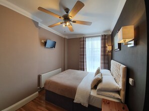A bedroom with a bed, a ceiling fan, a TV mounted on the wall, and a window with curtains. - Midway Guest House (Torquay)