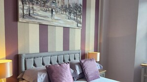 A bedroom with a bed, pillows, a nightstand, a lamp, a painting, and a wooden floor. - Midway Guest House (Torquay)