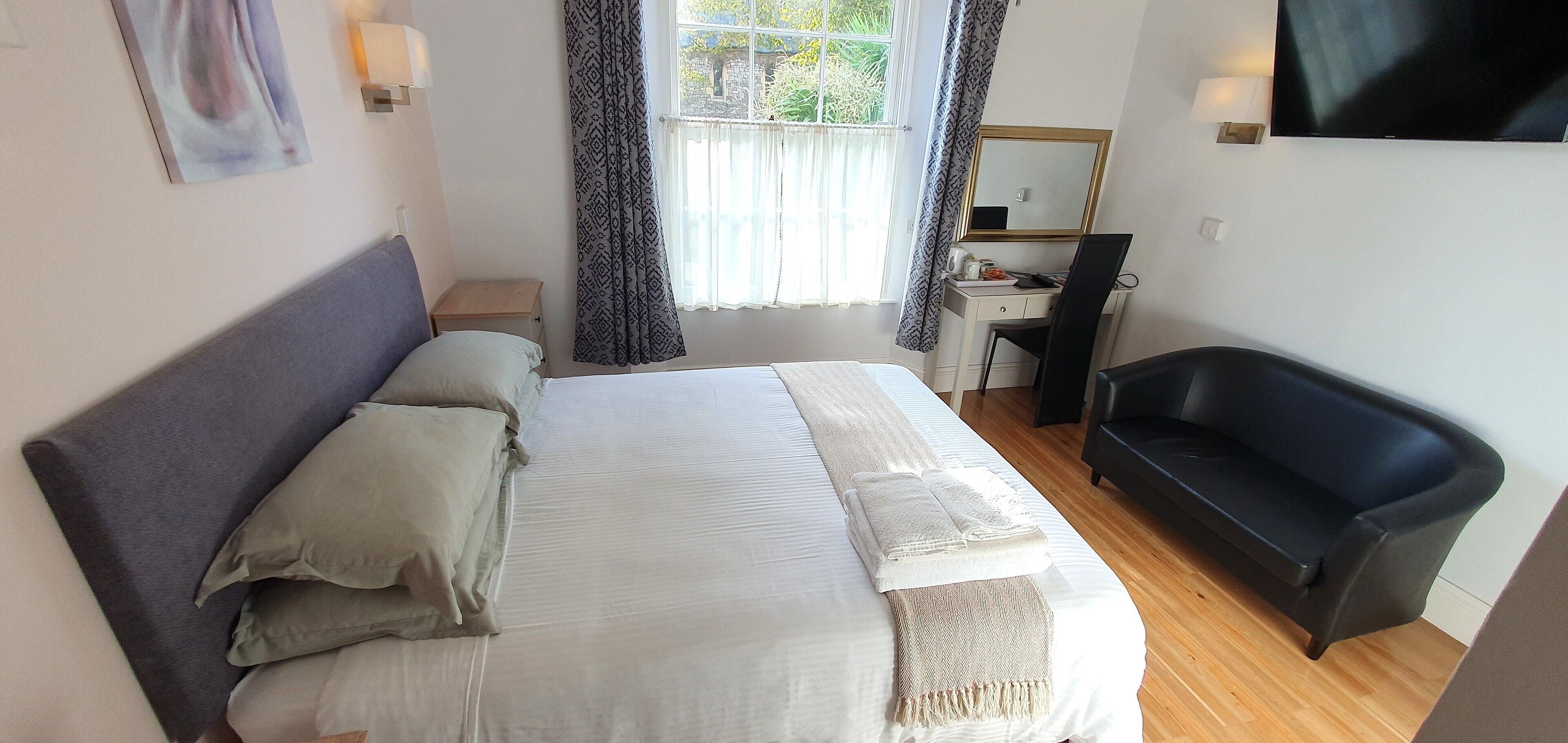A bedroom with a bed, a desk, a chair, a TV, and a sofa.