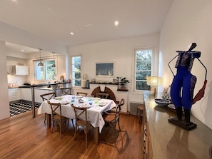Une cuisine moderne avec des meubles blancs, un coin repas avec une table dressée pour quatre personnes et une grande fenêtre qui laisse entrer la lumière naturelle.