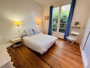 Une chambre à coucher avec un lit, des lampes de chevet, une fenêtre avec des rideaux, une petite table et une chaise.