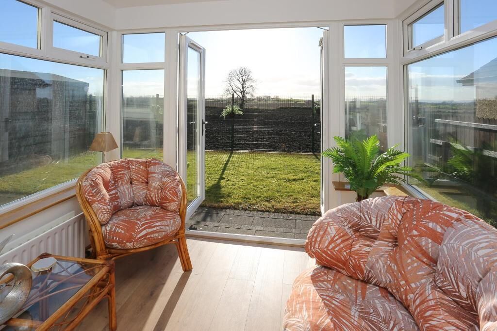 Una habitación soleada con ventanas amplias, una silla de madera, un sofá y una mesita.