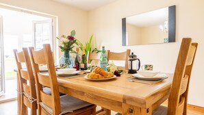A dining area with a wooden table, six chairs, a chandelier, and a large mirror on the wall. - The Ferns (Ballymoney)