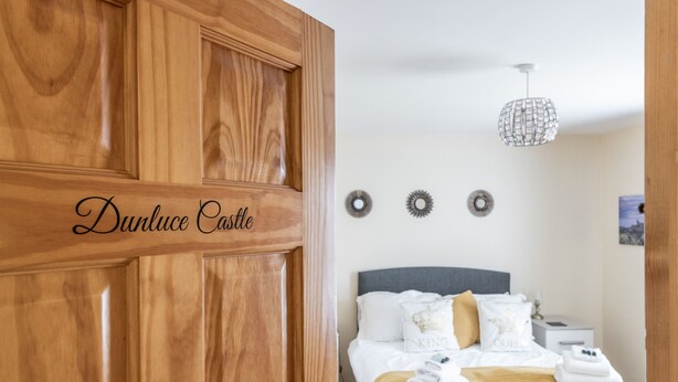 A hotel room with a wooden wardrobe, a bed with white bedding and a yellow throw, and a modern pendant light. - The Ferns (Ballymoney)