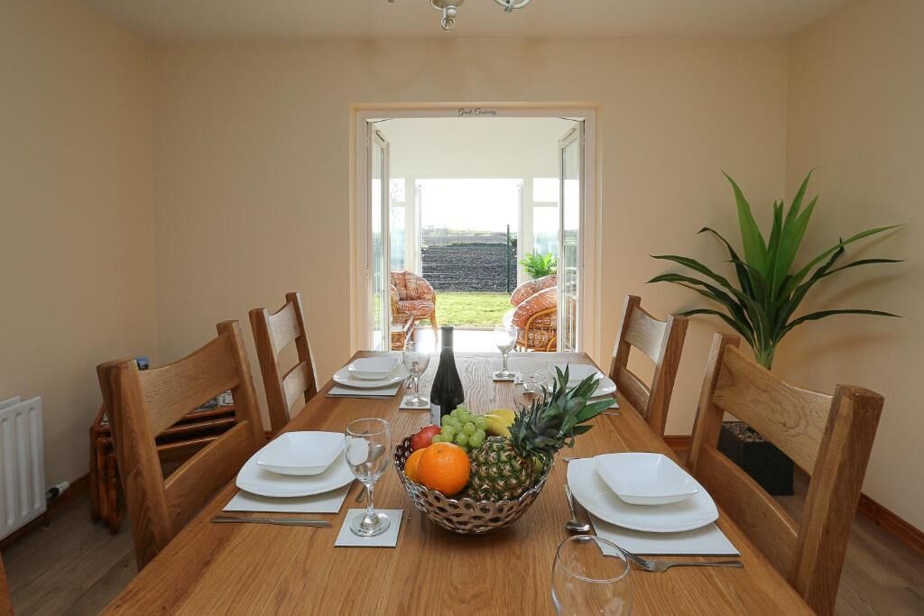 A dining room with a table set for four, a fruit bowl, and a view of the garden through an open door.