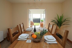 A dining room with a table set for four, a fruit bowl, and a view of the garden through an open door. - The Ferns (Ballymoney)