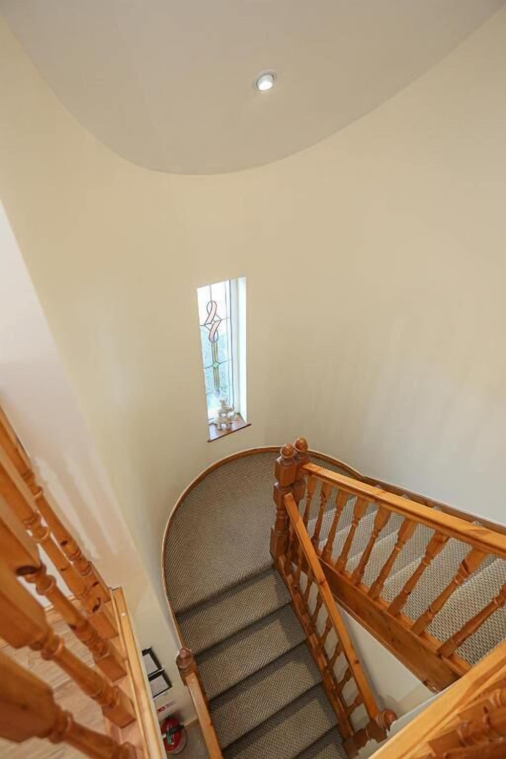 A curved staircase with wooden railings and a small window at the top.