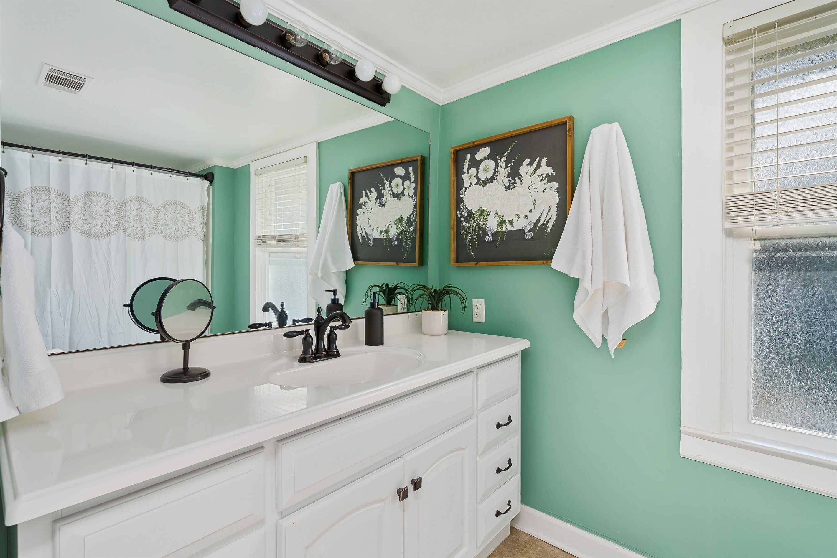 A bathroom with a white vanity, a large mirror, a white sink, and two framed floral artworks on the wall.