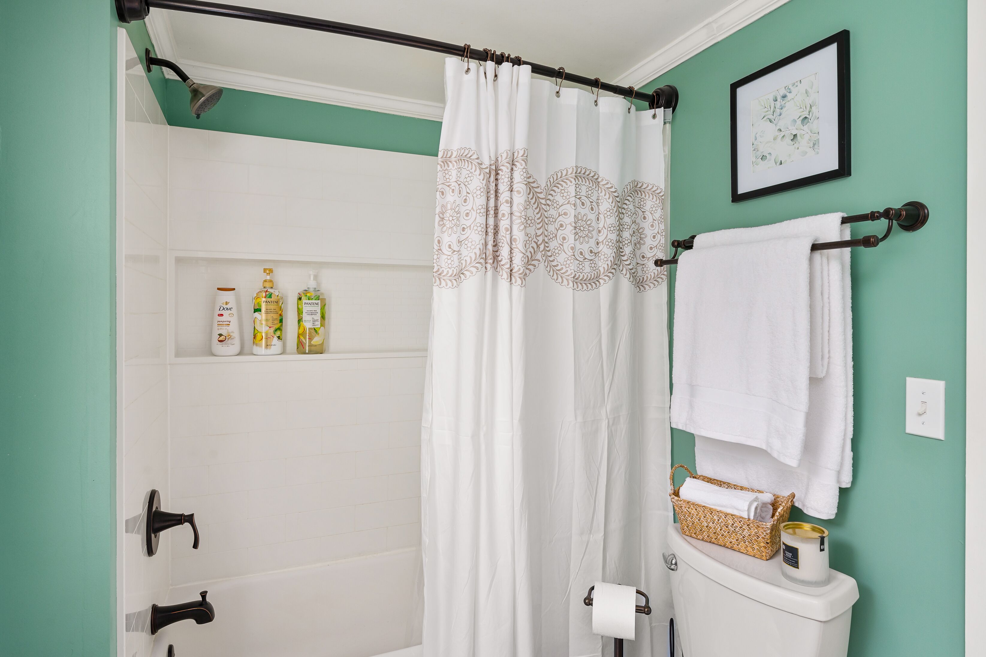 Une salle de bain avec un rideau de douche blanc, des toilettes blanches et une étagère contenant des articles de toilette.