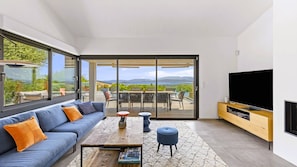 A modern living room with a sofa, coffee table, and TV, overlooking a deck with outdoor furniture. - Villa Arasu, 10 pers, piscine chauffée, vue mer, 15 mn à pieds plage (STE LUCIE DE PORTO VECCHIO)