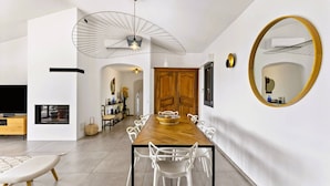 Un espace repas moderne avec une longue table en bois, des chaises blanches et un grand miroir au mur.