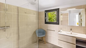 Une salle de bain moderne avec une douche à parois de verre, un lavabo avec un miroir et une fenêtre donnant sur un paysage verdoyant.