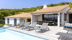 Un espace aménagé au bord de la piscine, avec des chaises longues, une table à manger et une vue sur une colline.