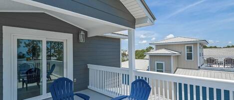A balcony with two blue chairs, a glass door leading to a patio, and a view of neighboring houses.