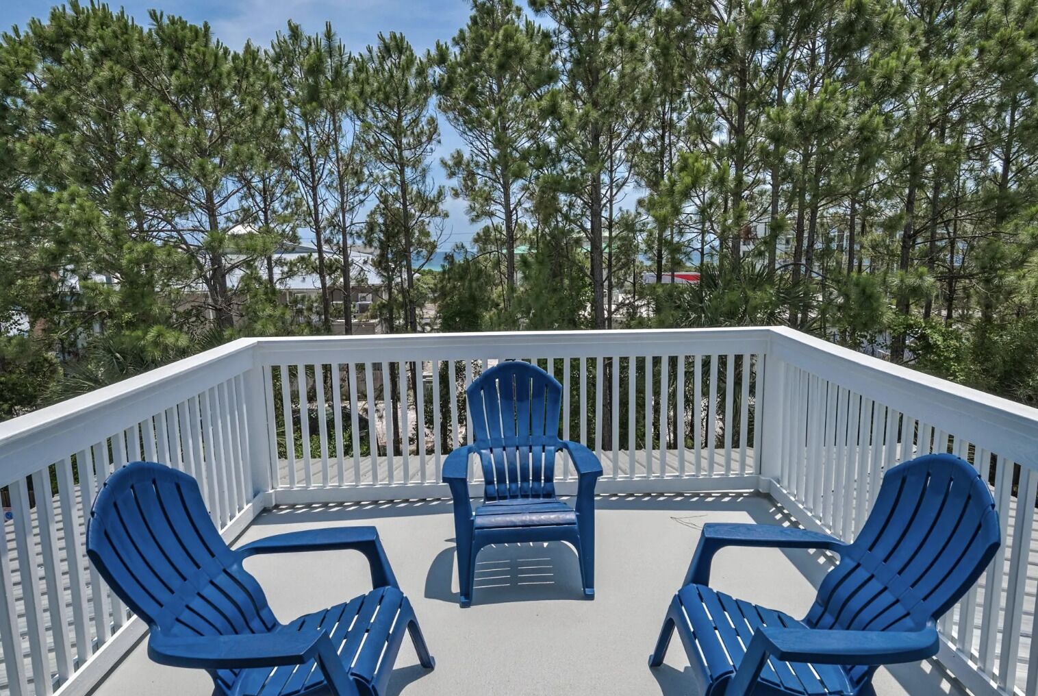 A deck with white railings and three blue Adirondack chairs.