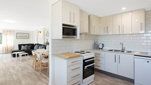 Une cuisine moderne avec des meubles blancs, un four à micro-ondes, une cuisinière, un four et un évier. Il y a également un coin repas avec une table et des chaises.