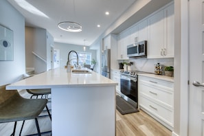 A modern kitchen with white cabinetry, a central island, stainless steel appliances, and a pendant light.