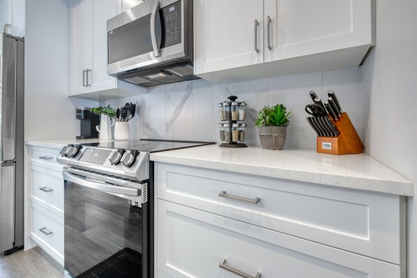 A modern kitchen with stainless steel appliances, white cabinetry, and a countertop with kitchen tools and a plant.
