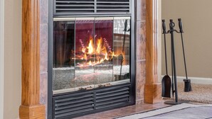 A fireplace with a glass front, flanked by wooden columns, and a broom and candelabra to the right.